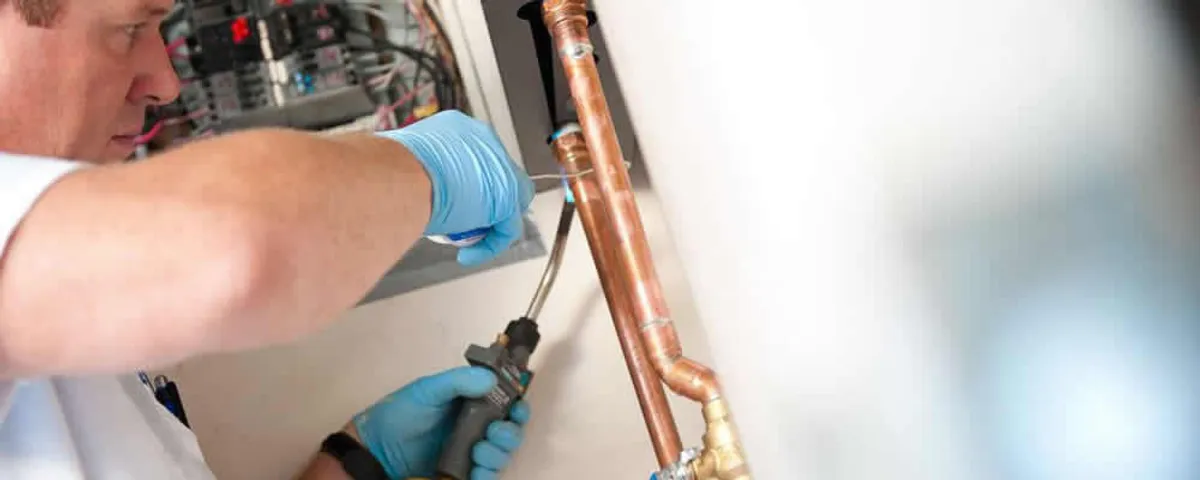 Water heater repair technician testing copper pipe connections and controls in Ogden, UT